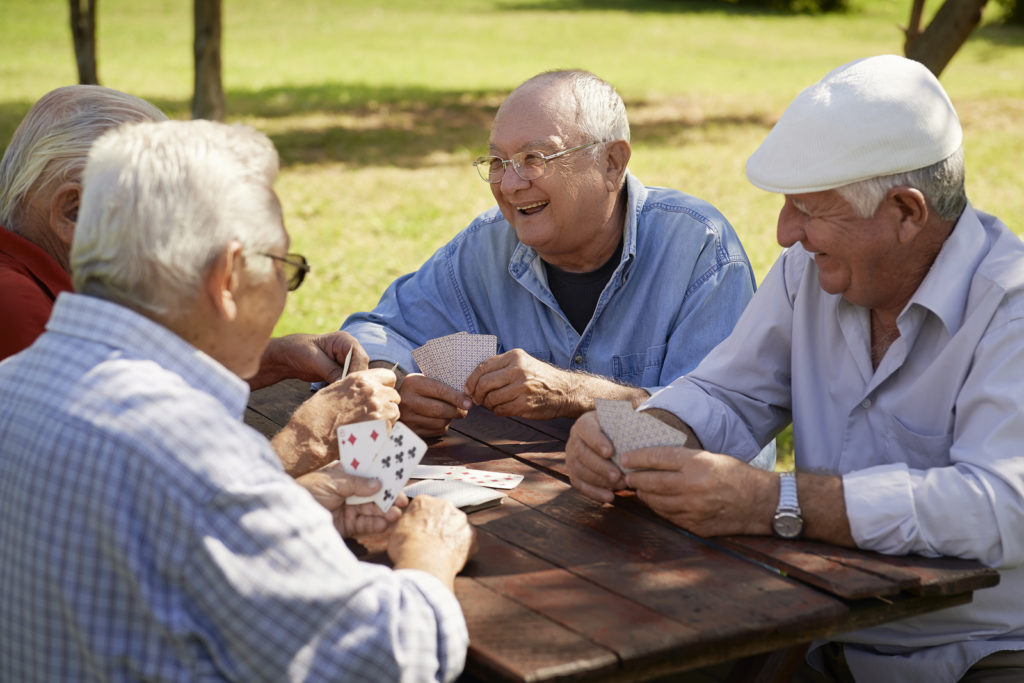 Active retirement old people and seniors free time group of four elderly men having fun and playing cards game at park. Waist up